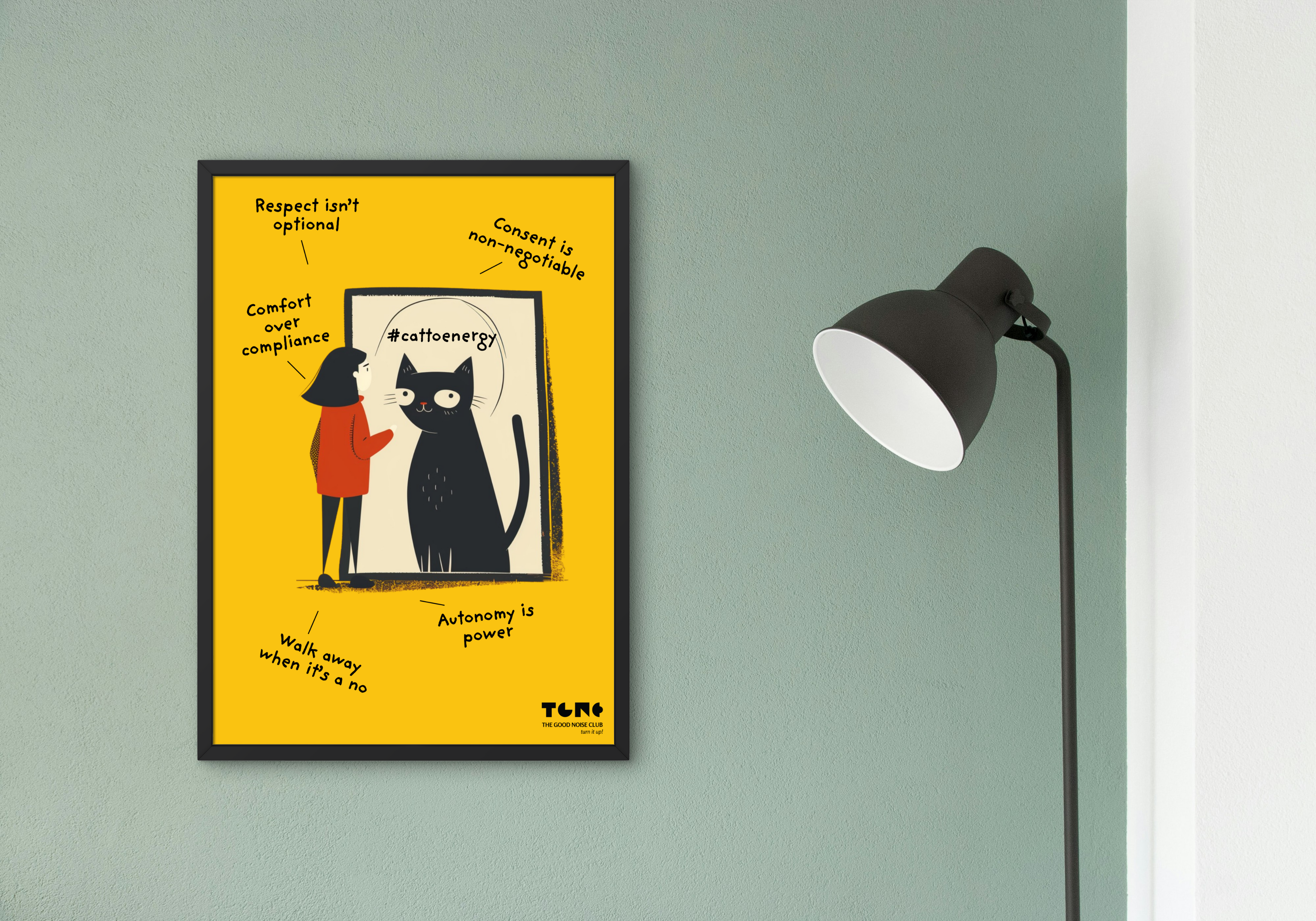 Framed artwork with a black cat on a yellow background, mounted on a green wall next to a lamp.