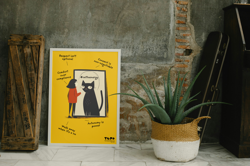 Poster with a black cat illustration on a yellow background, placed against a textured wall with a plant and wooden crate.