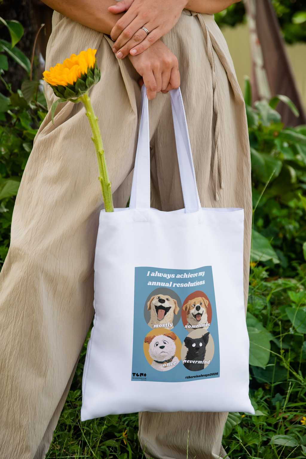 Person holding a tote bag with dog illustrations and text, standing outdoors.