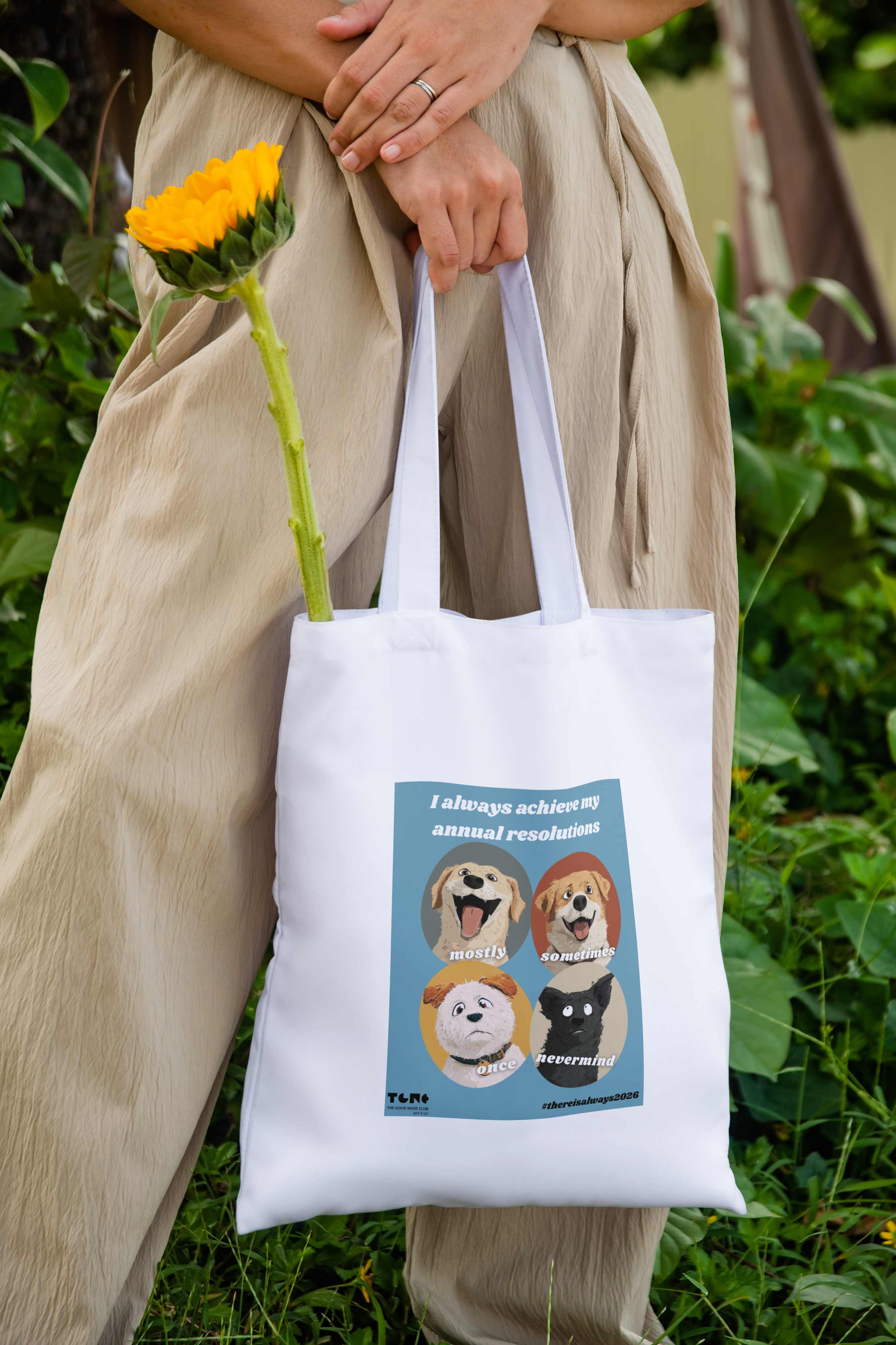 Person holding a tote bag with dog illustrations and text, standing outdoors.