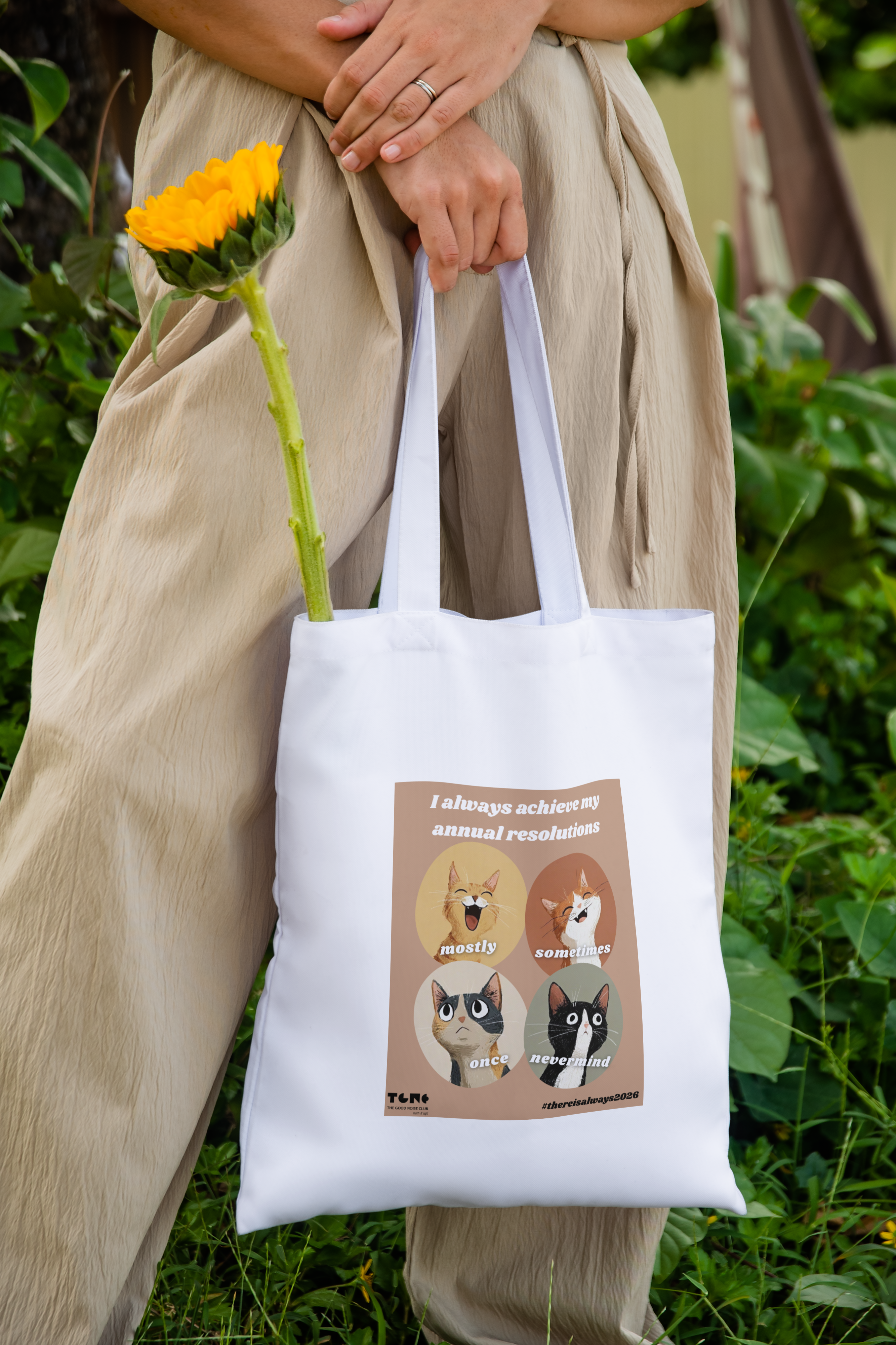 Person holding a tote bag with cat illustrations and text, standing outdoors.