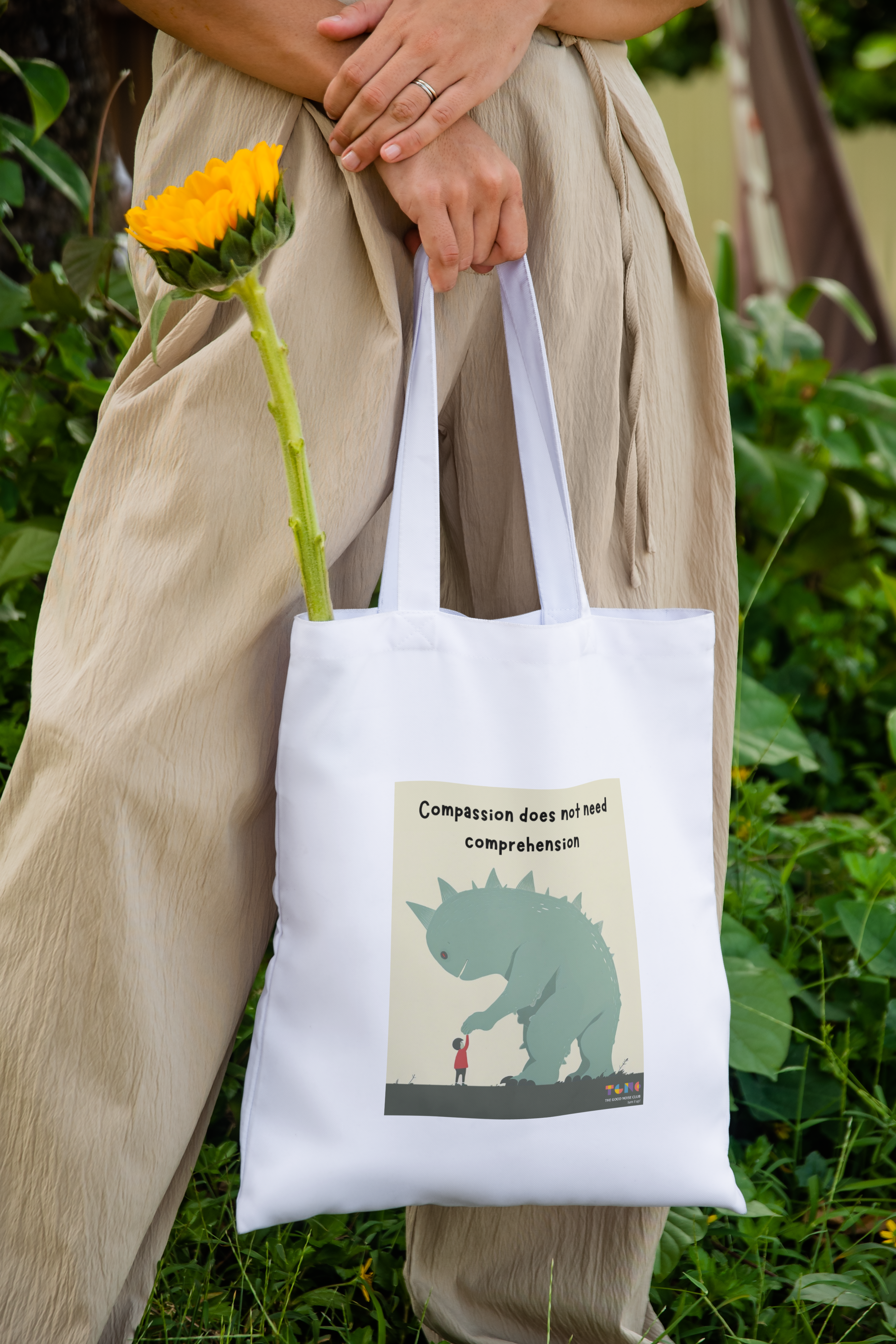 Person holding a tote bag with a graphic design of a triceratops and text, standing outdoors.