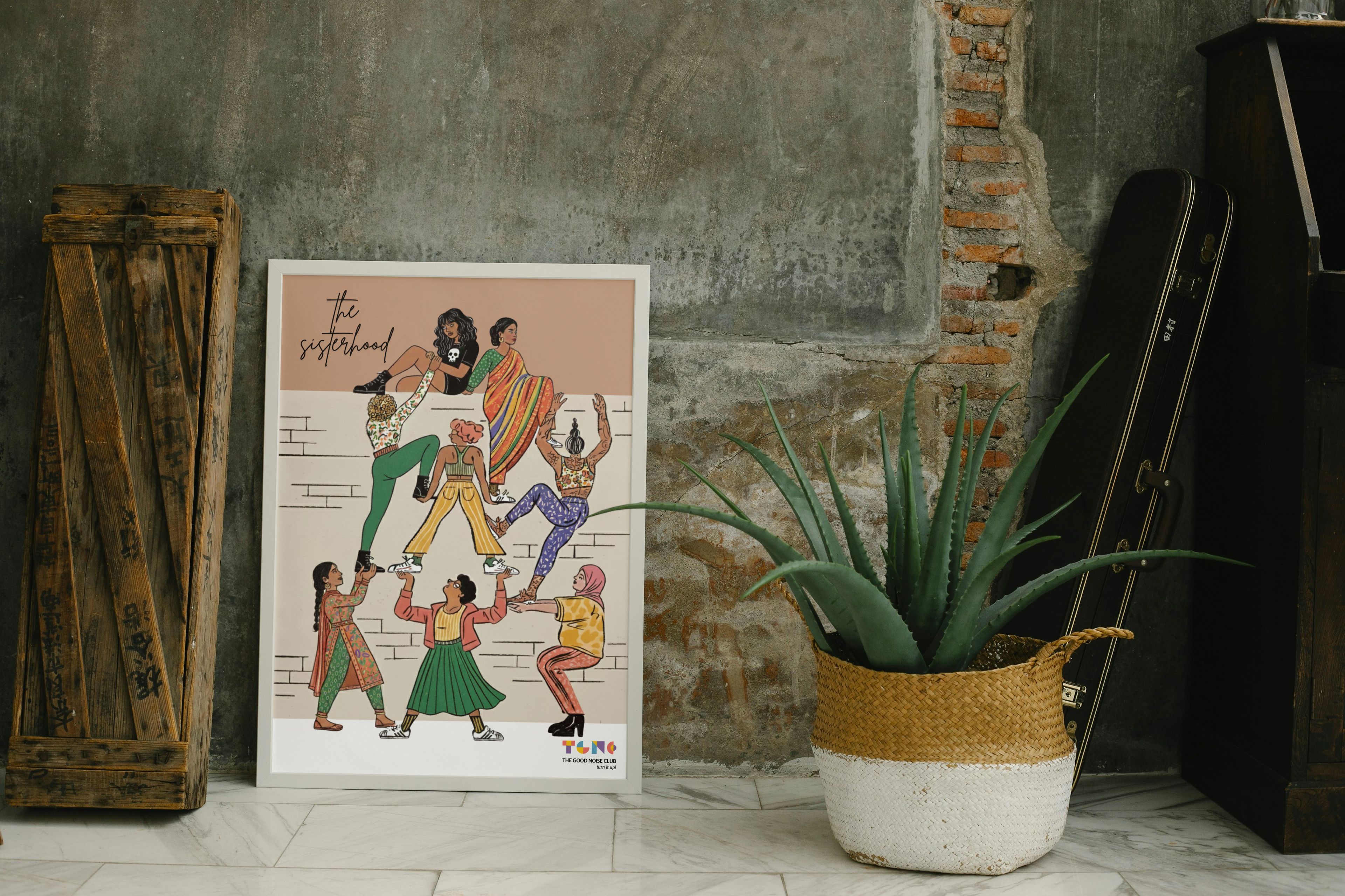 Poster of a colorful illustration of people on a wall next to a plant and wooden crate.
