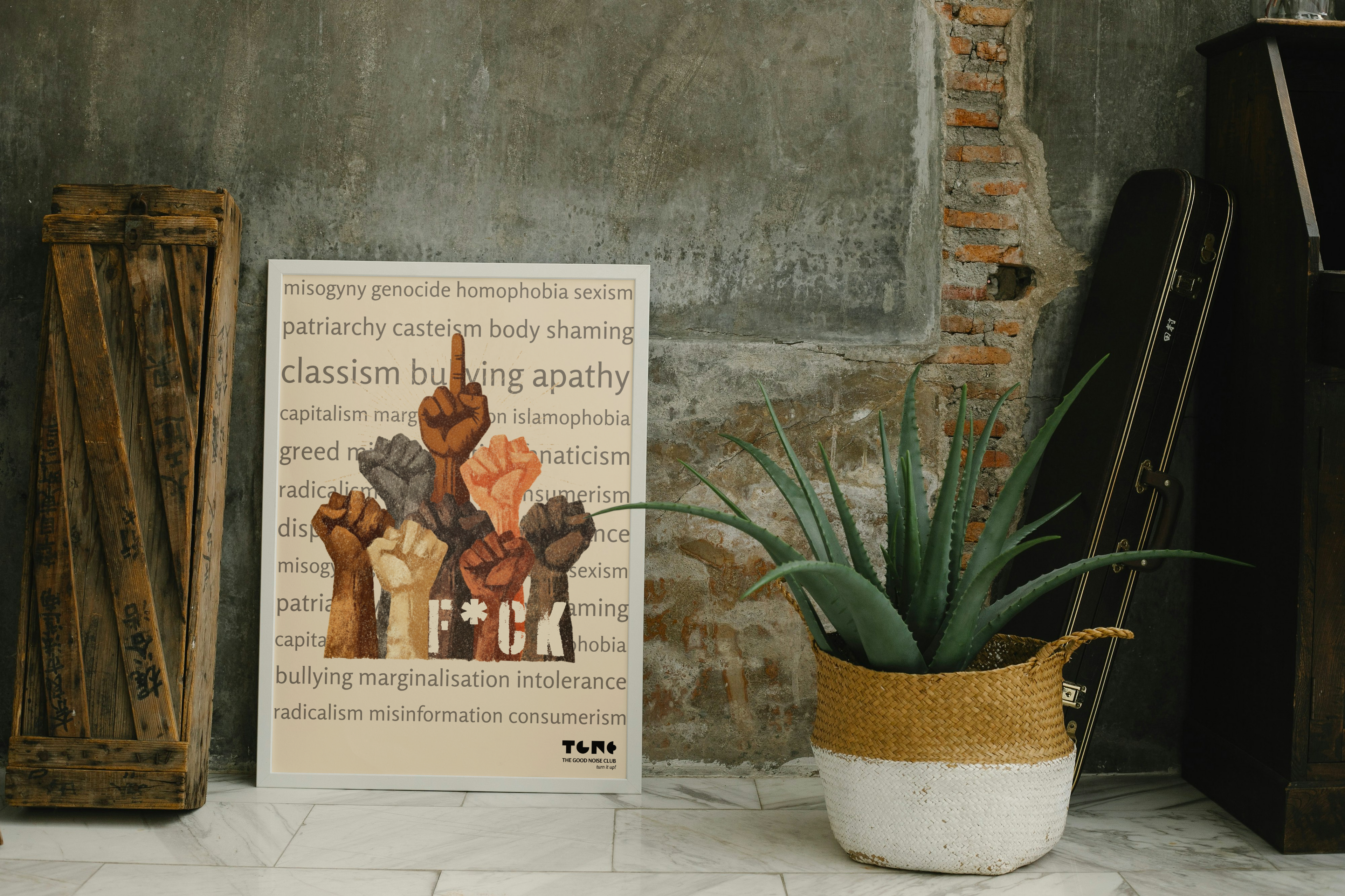 Poster with abstract art and text on a textured wall with a plant and wooden crate.