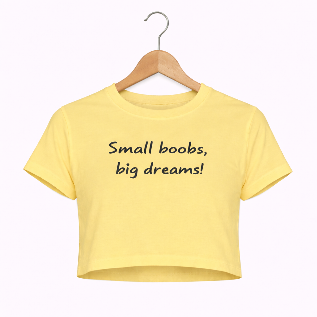 Yellow crop top with 'Small boobs, big dreams!' text on a hanger against a white background