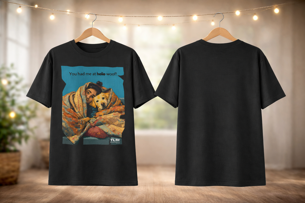 Black t-shirt with a graphic of a dog wrapped in a blanket and text, displayed on hangers against a neutral background.