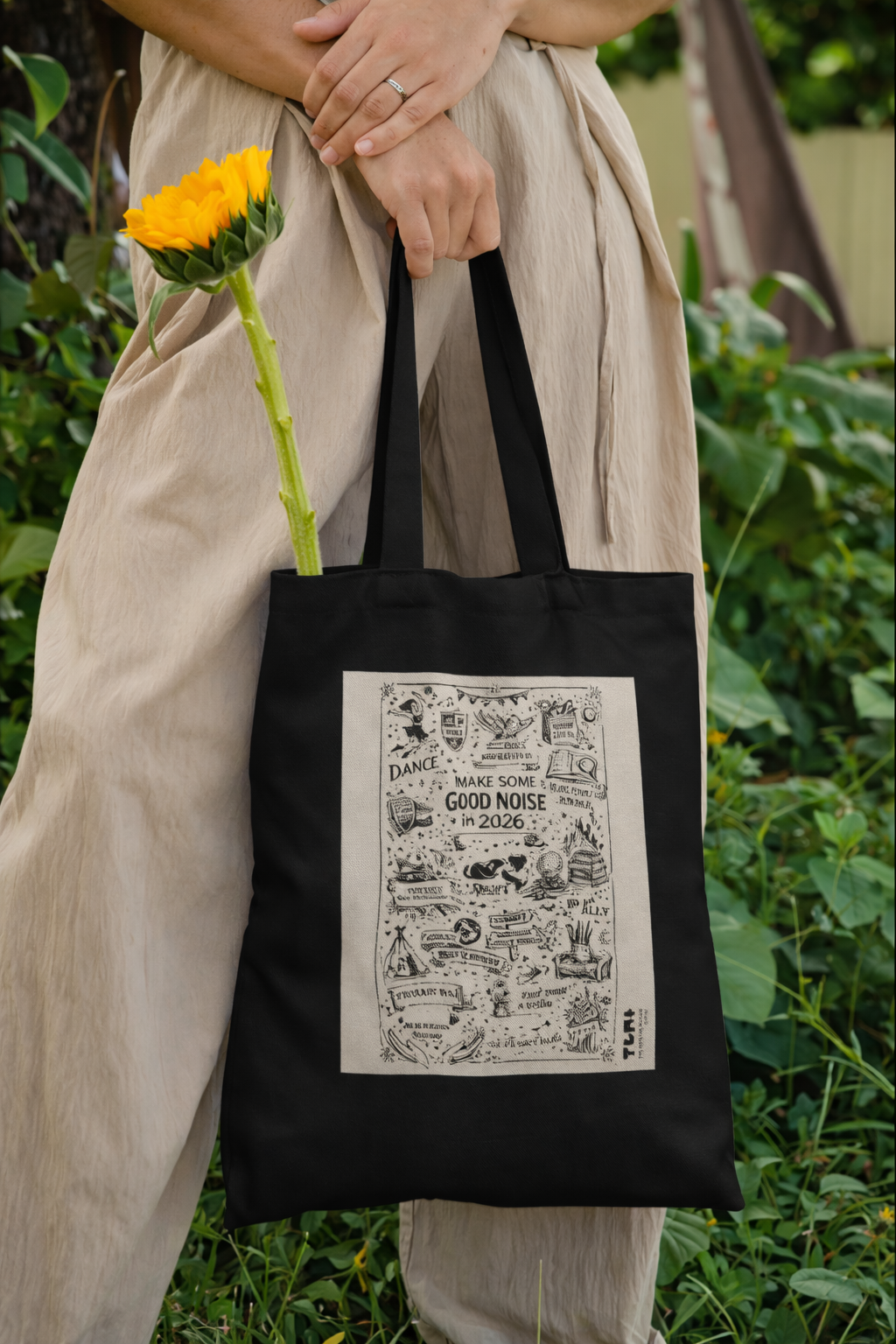 Person holding a black tote bag with a printed design, outdoors.