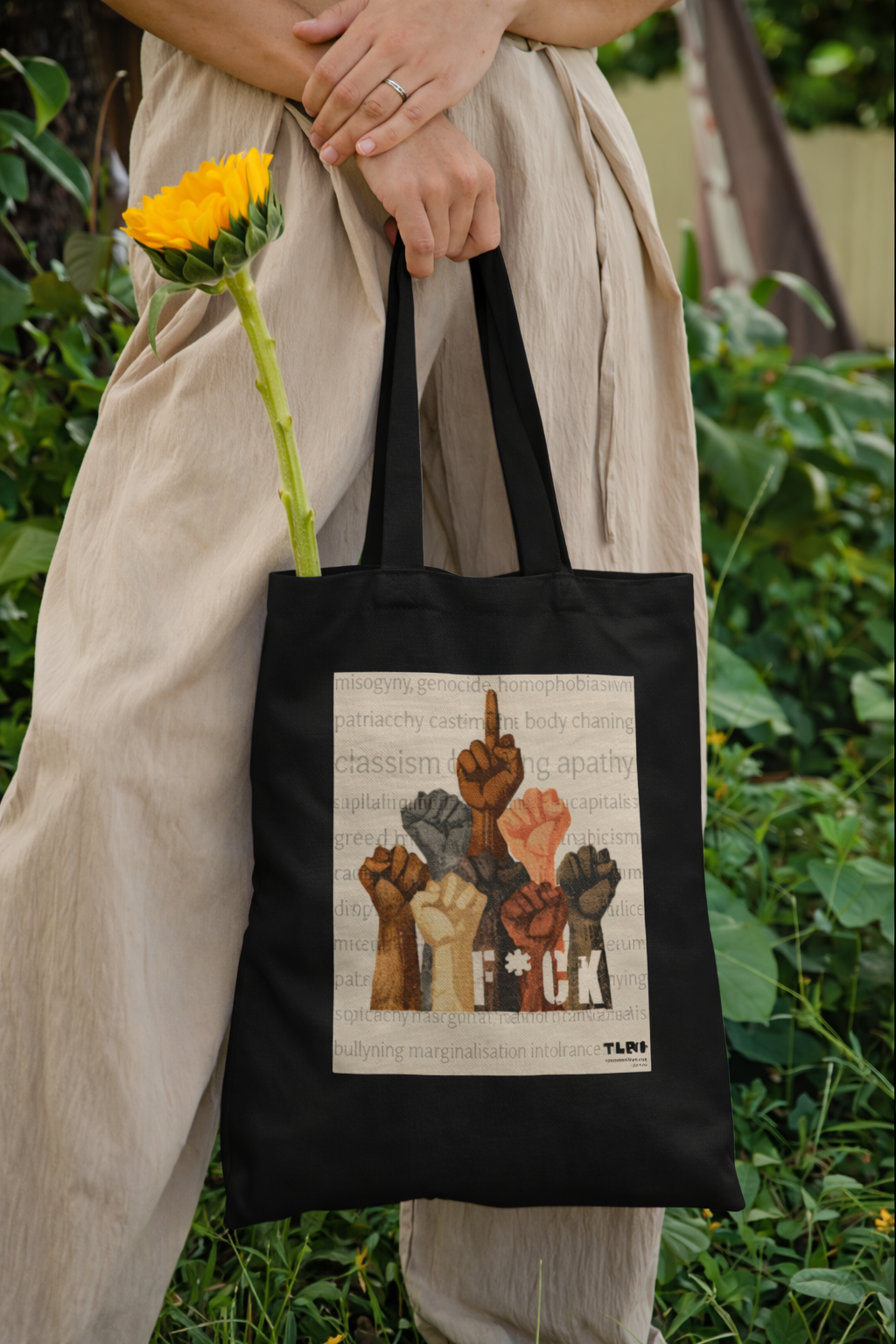 Person holding a black tote bag with a graphic design in a natural setting