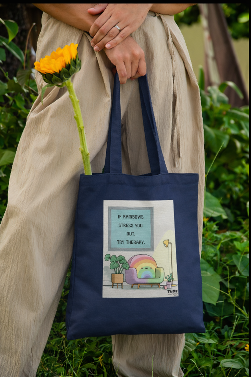 Person holding a tote bag with a colorful design and text, standing outdoors.