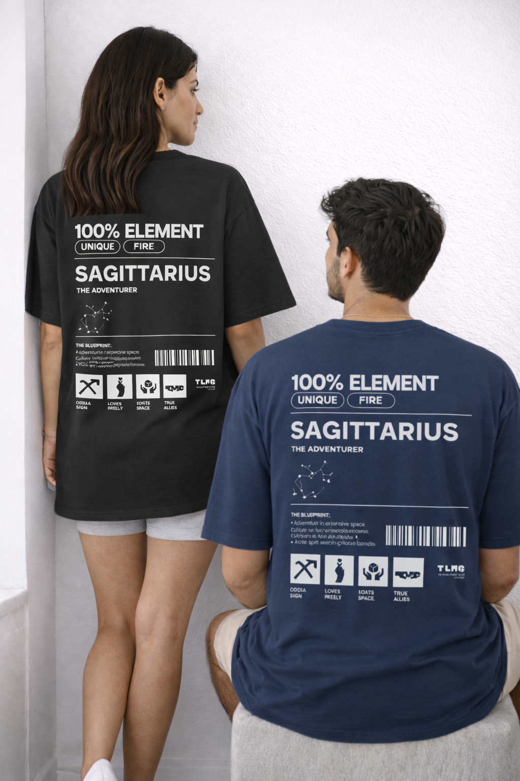 Two people wearing t-shirts with zodiac design on the back, standing against a white wall.