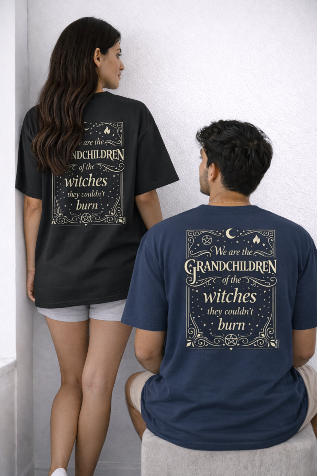 Two people wearing t-shirts with text on the back, standing against a white wall.