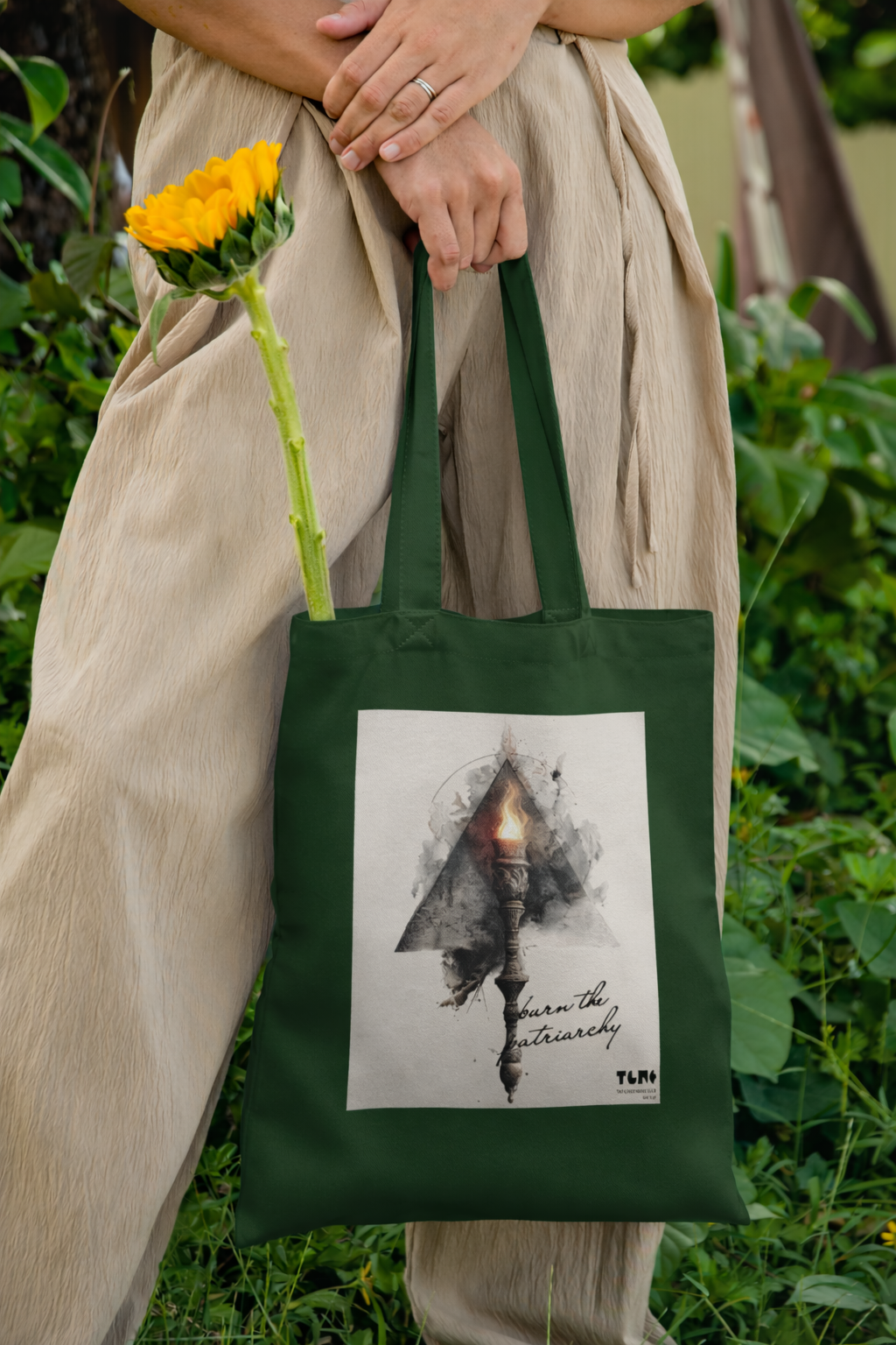 Person holding a green tote bag with a design and sunflowers outdoors