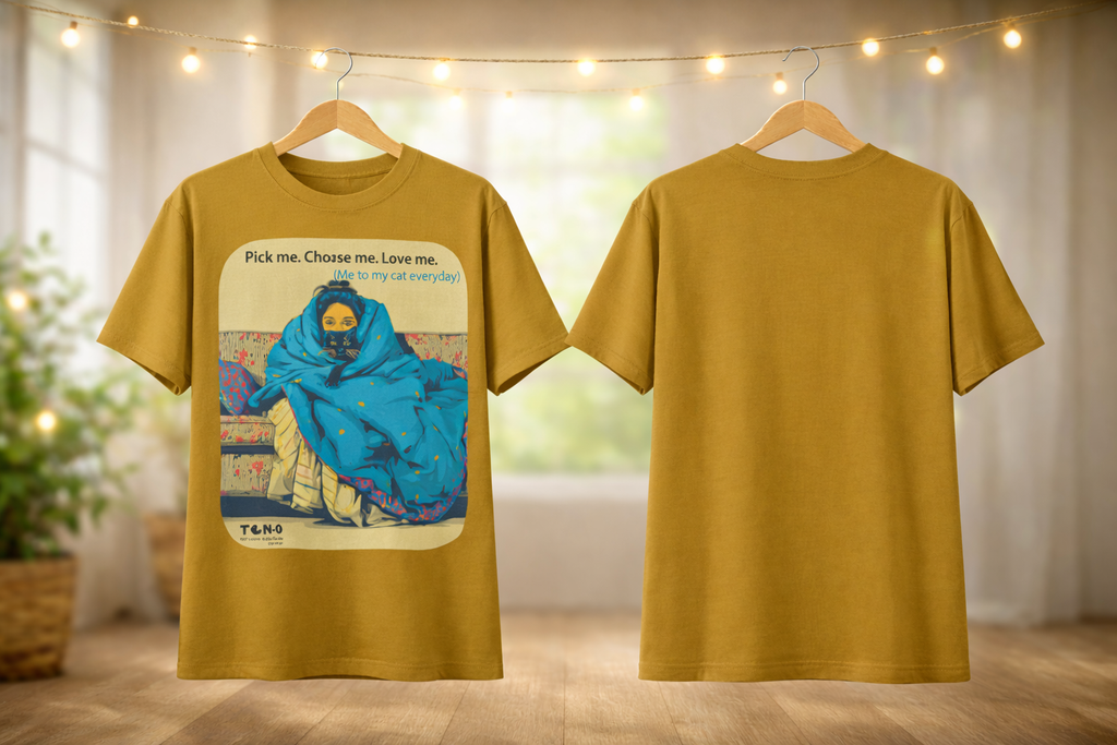 Mustard yellow t-shirt with a graphic design on a wooden floor with blurred lights in the background