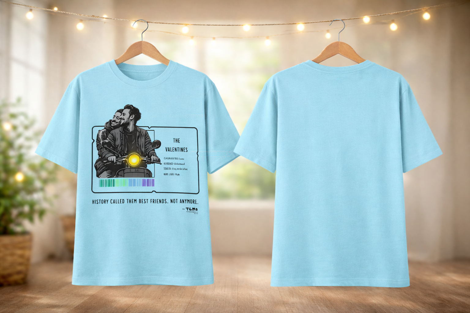 Light blue t-shirt with graphic design on a wooden floor with string lights in the background