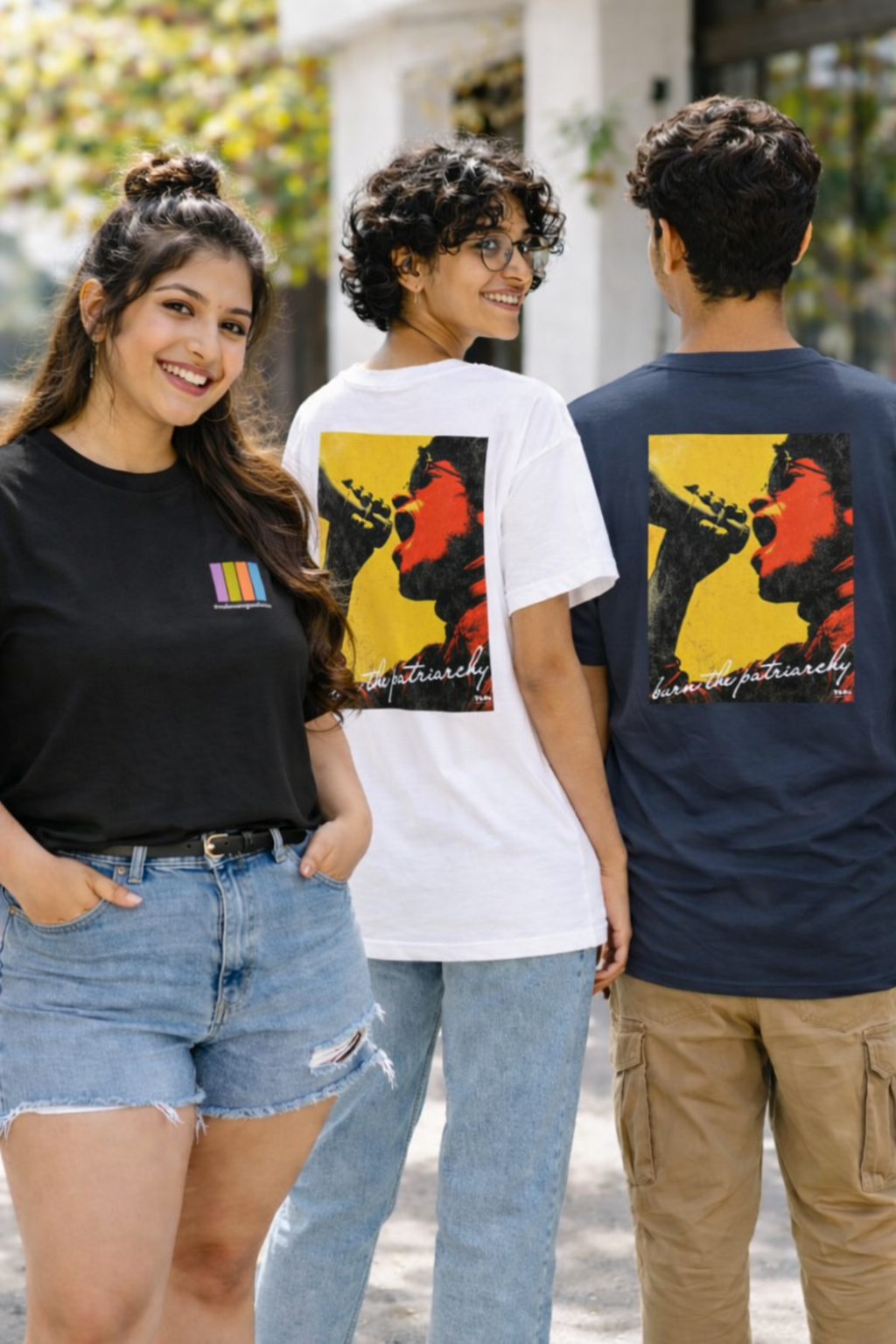 Three people wearing t-shirts with artistic designs on the back, standing outdoors.
