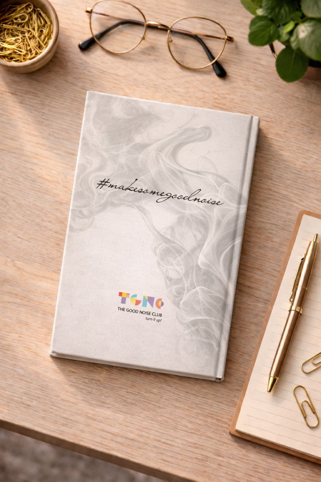 Notebook with decorative cover on a wooden surface with glasses and stationery items.