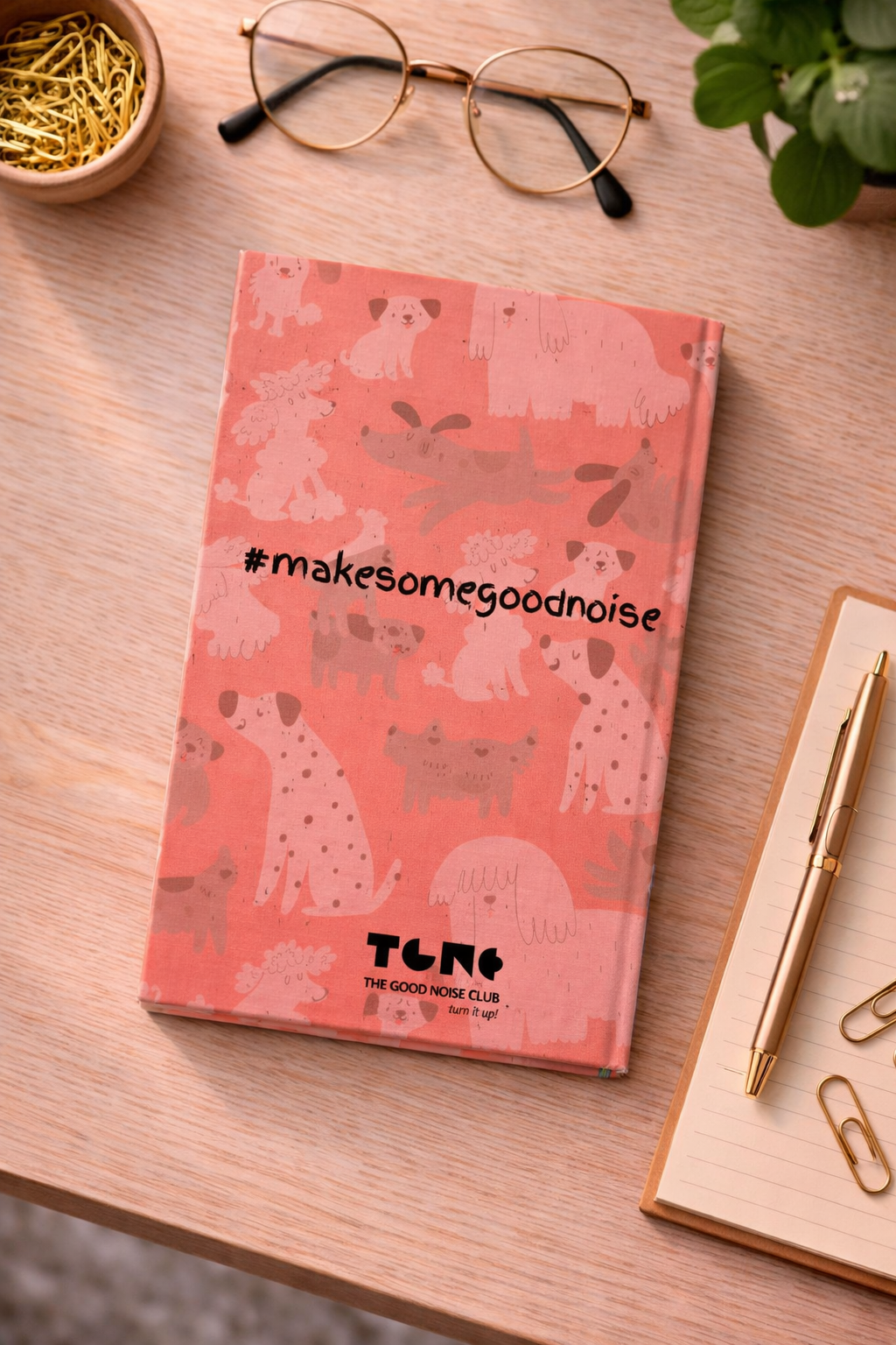 Notebook with animal pattern and '#makesomegoodnoise' text on a wooden surface with glasses and a pen.