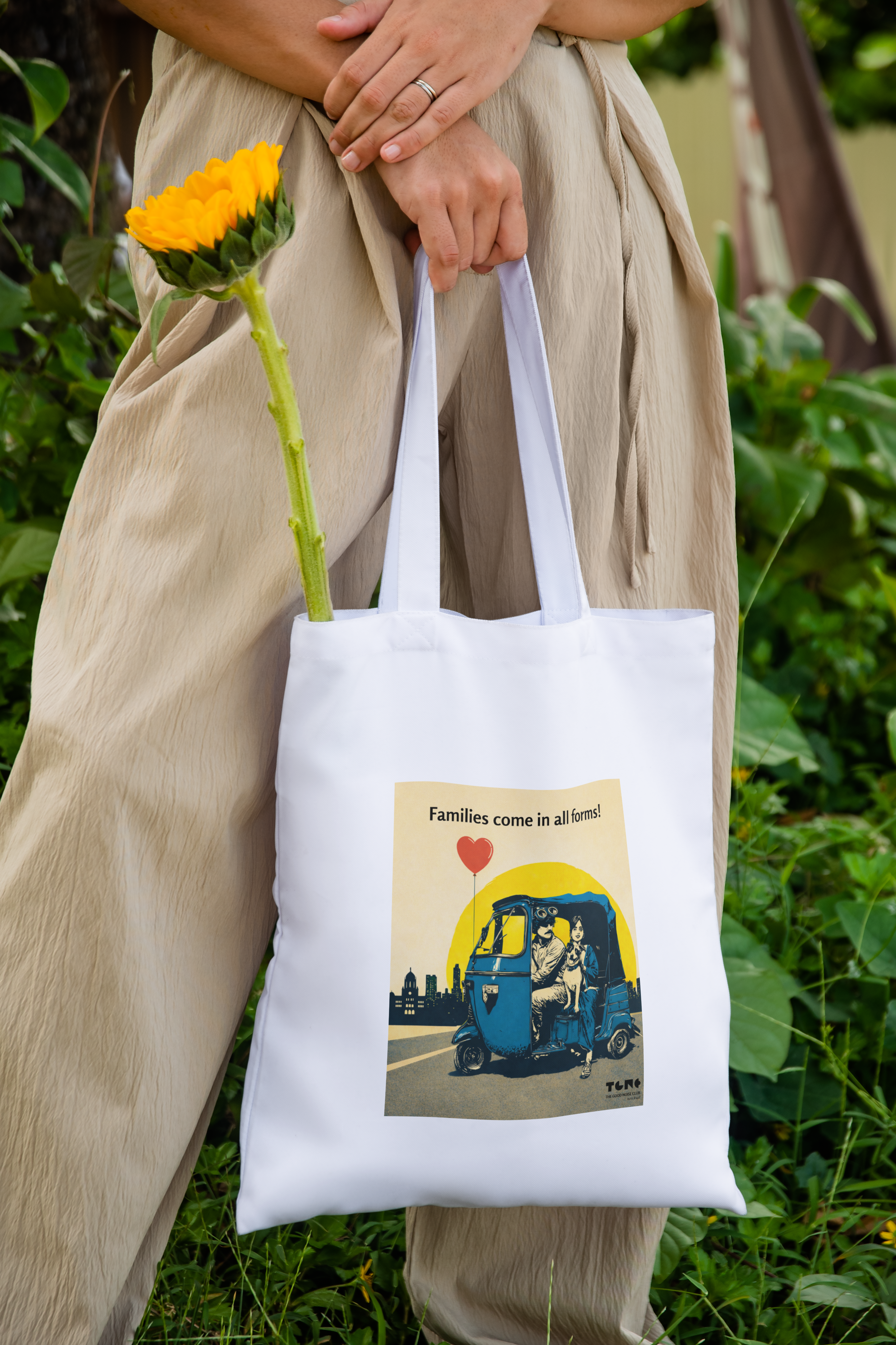 Person holding a white tote bag with a printed design, standing outdoors with greenery.