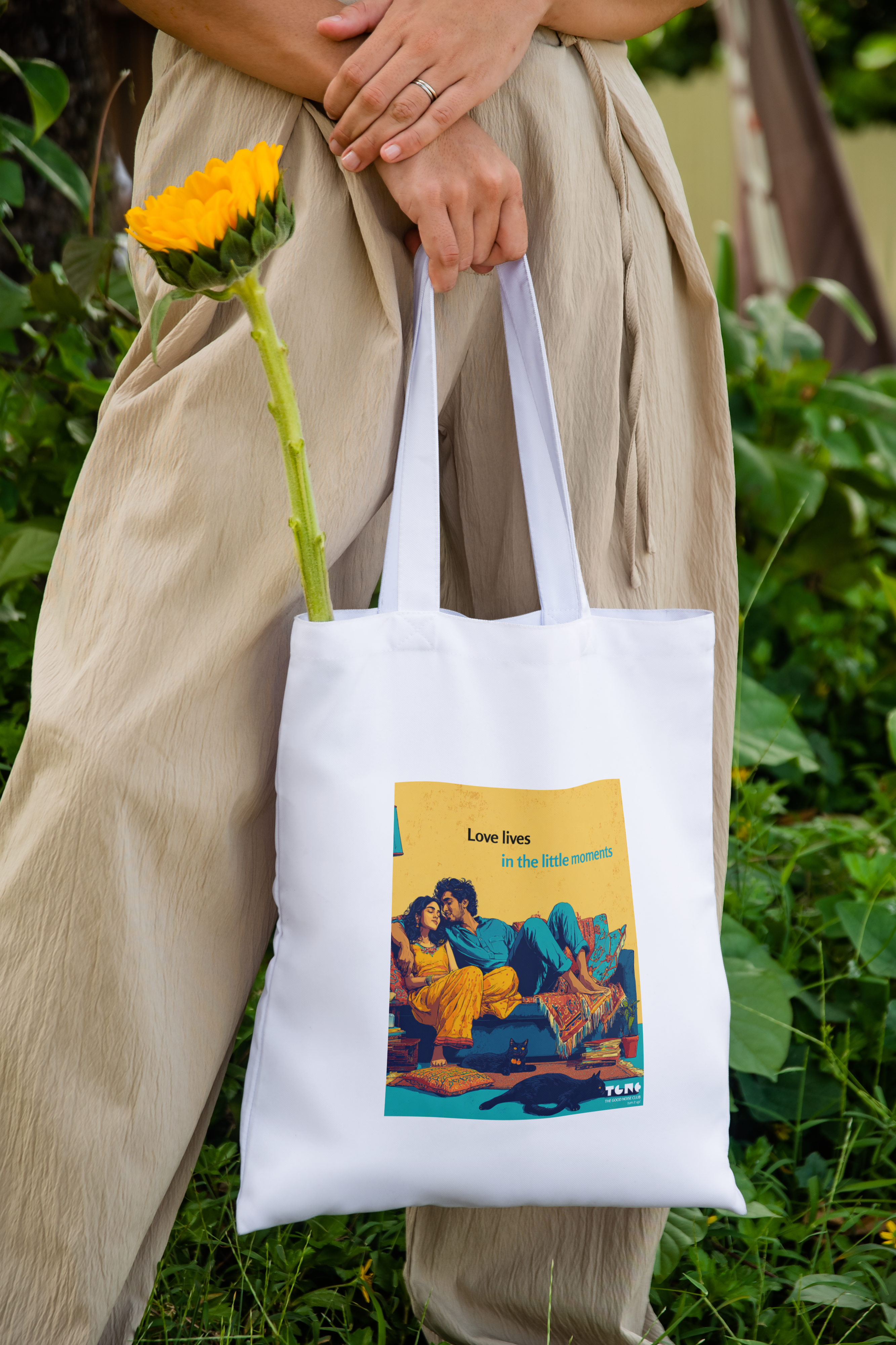 Person holding a white tote bag with a design, standing outdoors with greenery.