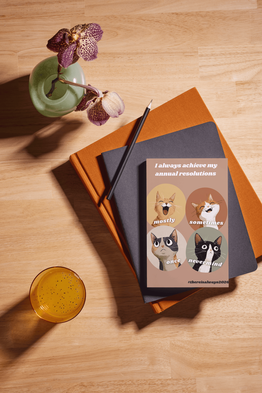 Notebooks with a cat-themed bookmark on a wooden surface with a drink and flowers.