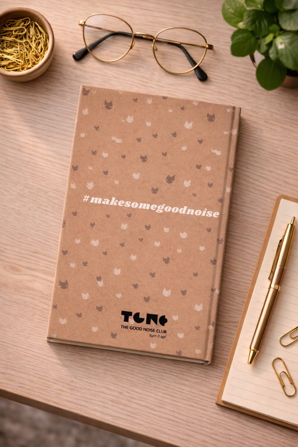 Notebook with 'makesomegoodnoise' branding on a wooden surface with glasses and a pen.