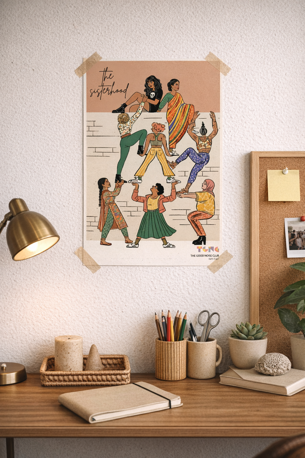 Poster of women lifting each other up over  a wall above a desk with stationery items.