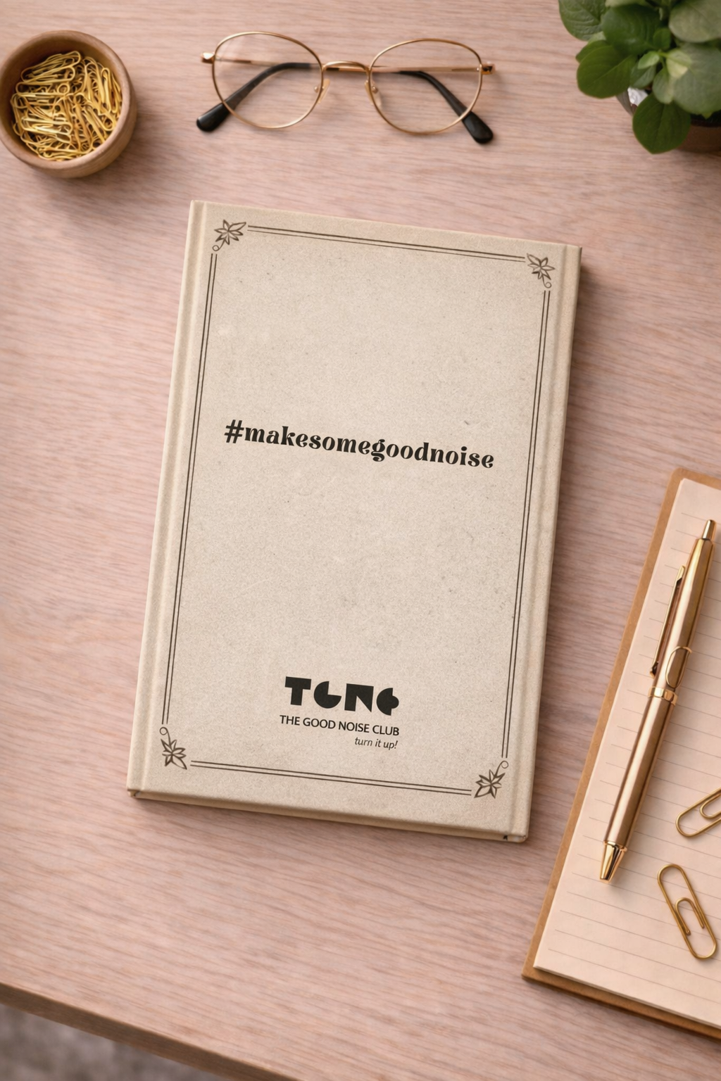 Notebook with '#makesomegoodnoise' text on a wooden surface with glasses and a pen.